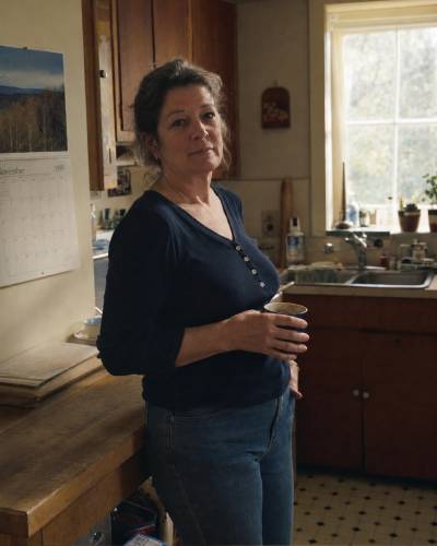 A 55-year-old woman holding a coffee mug in a 1995 kitchen with a November calendar on the wall — specific era, specific person, deliberate
